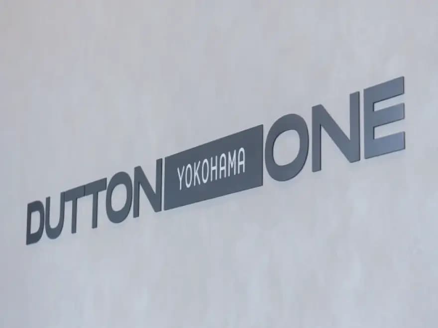 白い壁面にシンプルに配置されたDUTTON YOKOHAMA ONEのロゴ看板