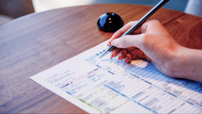 輸入車ディーラーでの商談時にテーブル上の書類にペンで記入している手元の様子