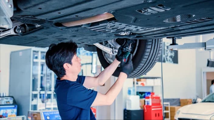 リフトアップされた中古車の下から足回りの点検作業を行うメカニックの姿