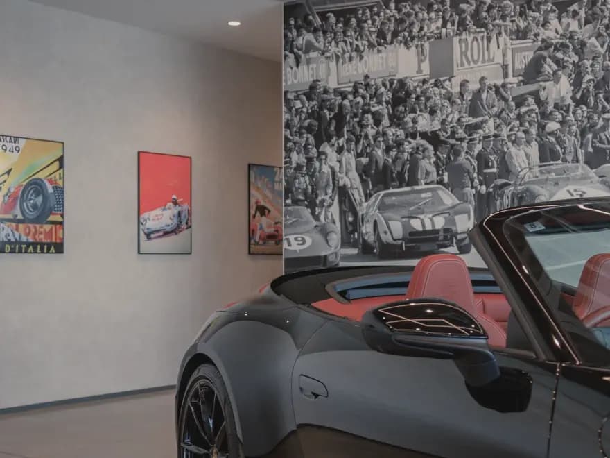 ショールーム内に展示された赤色シートの黒いポルシェと壁面のレース写真パネル