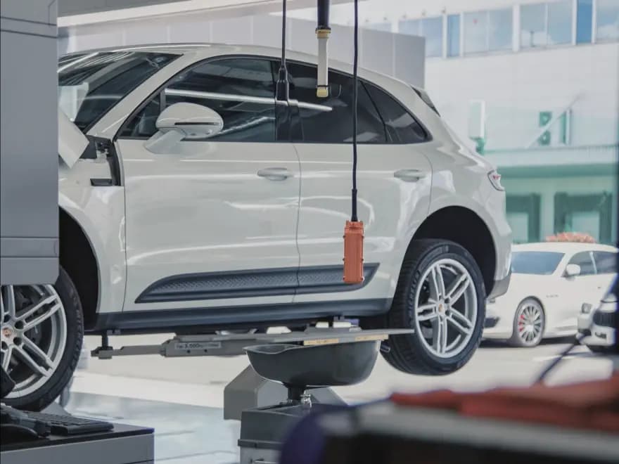 整備工場のリフトで持ち上げられメンテナンスを受けている白いSUVの輸入車