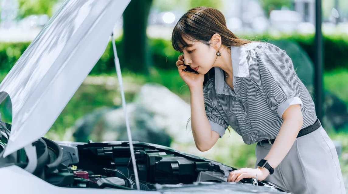 外出先で車のボンネットを開けて電話で助けを求める女性と輸入車